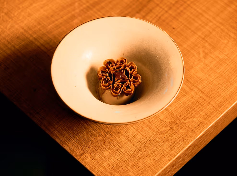 Toasted barley gelato topped with a crisp sesame rosette in a pale ceramic bowl